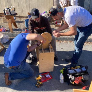 Adults working around a wooden piece of Faire equipment with tools scattered about.