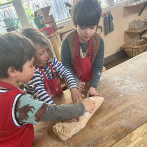 three kindergarten children are kneading dough at a table while wearing aprons
